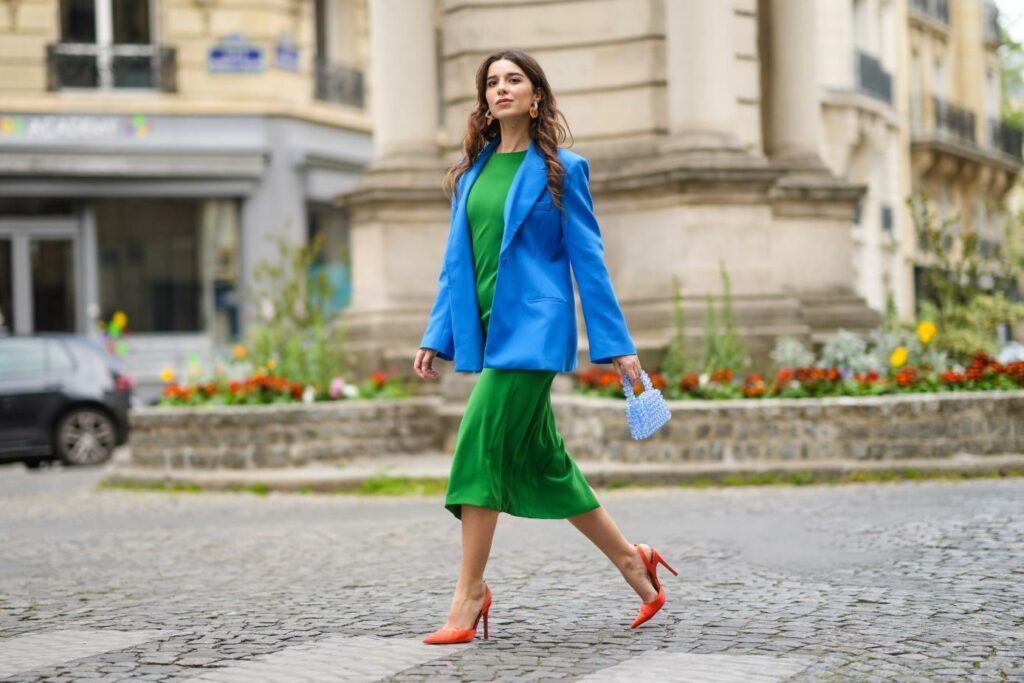 Moteris, dėvinti žalią suknelę, mėlyną švarką ir oranžinius aukštakulnius