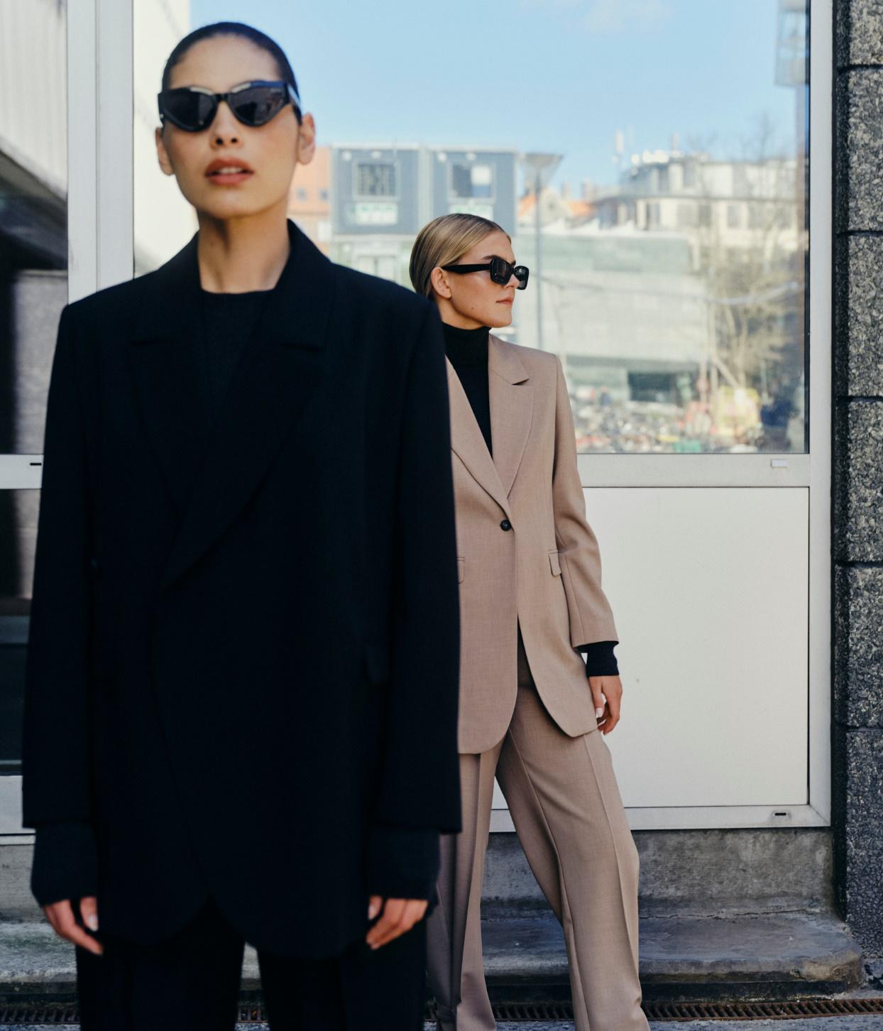 Dvi moterys - viena vilki juodą, kita - smėlio spalvos kostiumėlį