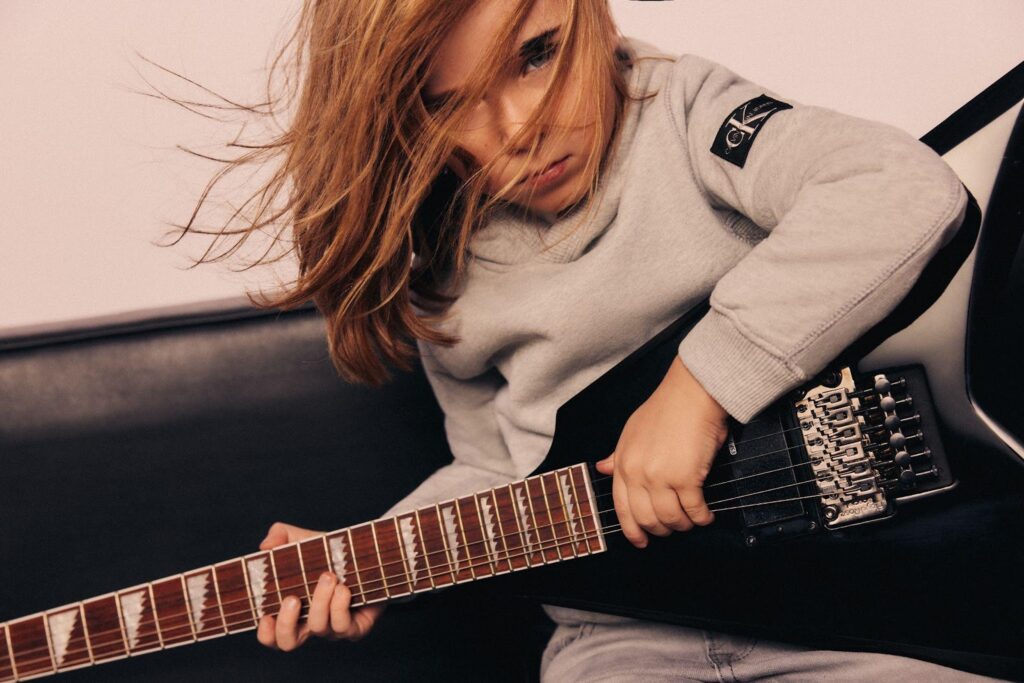 Berniukas groja gitara vilkėdamas pilką Calvin Klein Jeans megztinį