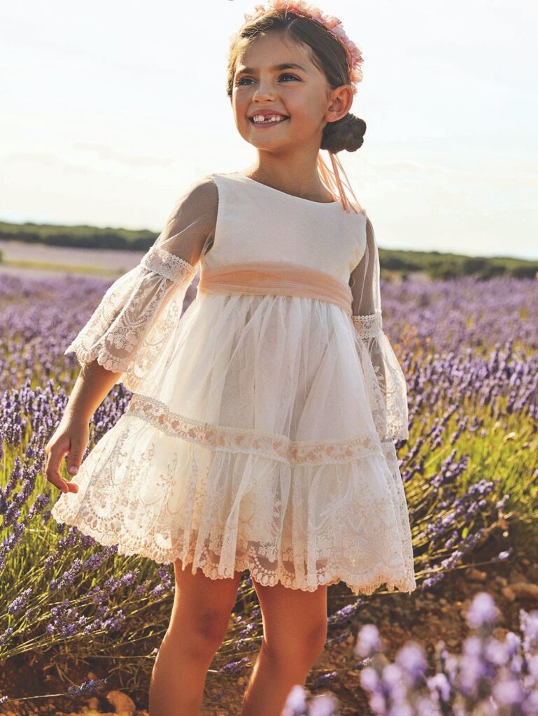 Maža mergaitė, dėvinti trumpa balta nėriniuota Abel&Lula suknele pūstomis rankovėmis