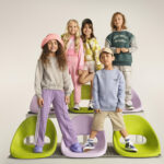 5 vaikai, pozuojantys ant spalvingų kėdžių