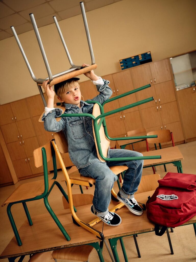 Berniukas, dėvintis džinsines kelnes ir marškinius laiko kėdę ant galvos