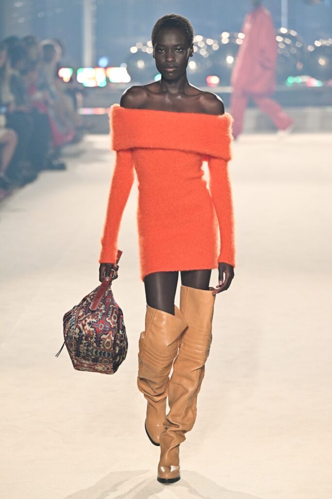 Modelis, dėvinti oranžinę suknelę ir ilgus rudus ilgaaulius batus