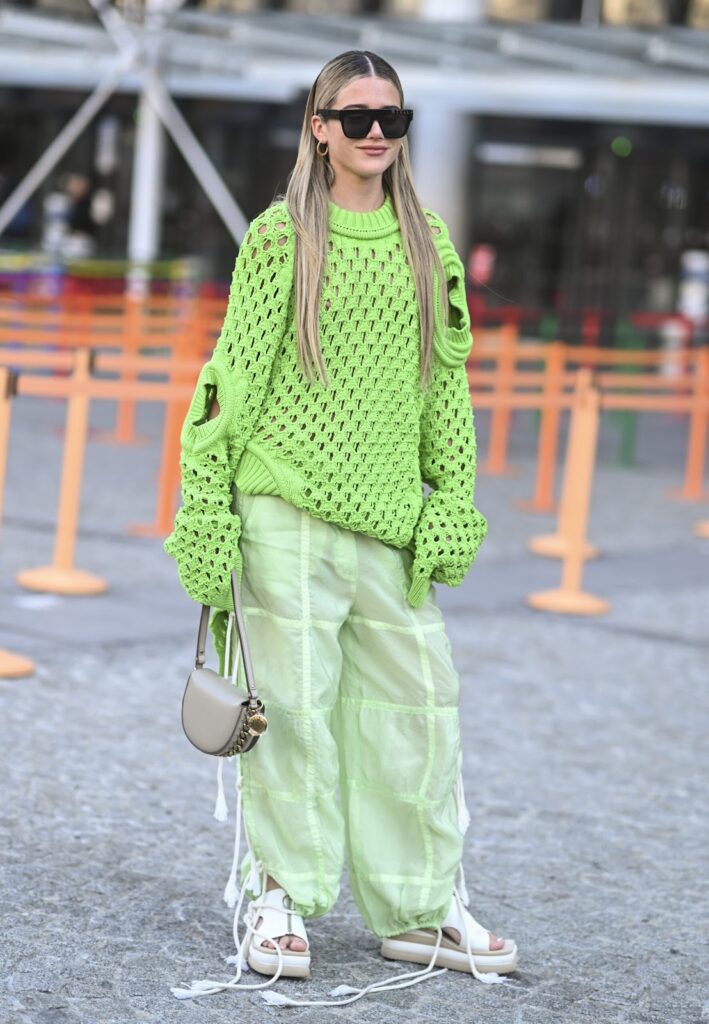 Mergina, apsirengu žaliosios citrinos atspalvio megztiniu su skylėmis ir plačiomis kelnėmis