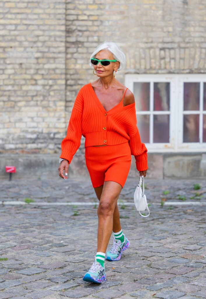 Moteris, dėvinti trumpą oranžinį sijoną, oranžinį kardiganą ir sportbačius