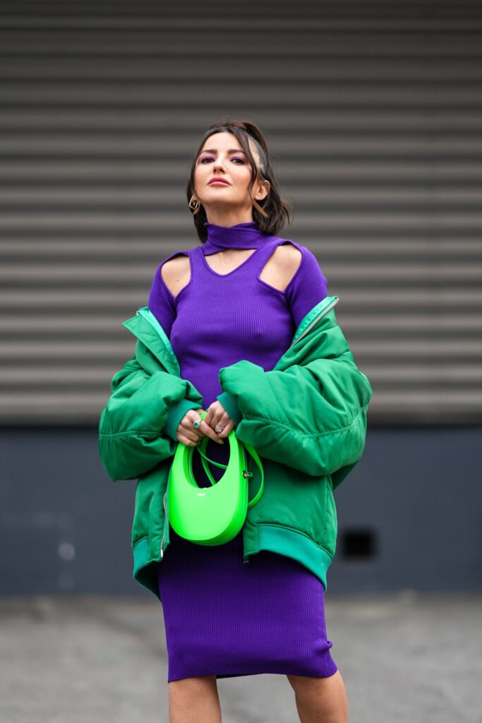 Nuomonės formuotoja, apsirengusi aptempta violetine suknele ir žalia pūkine striuke