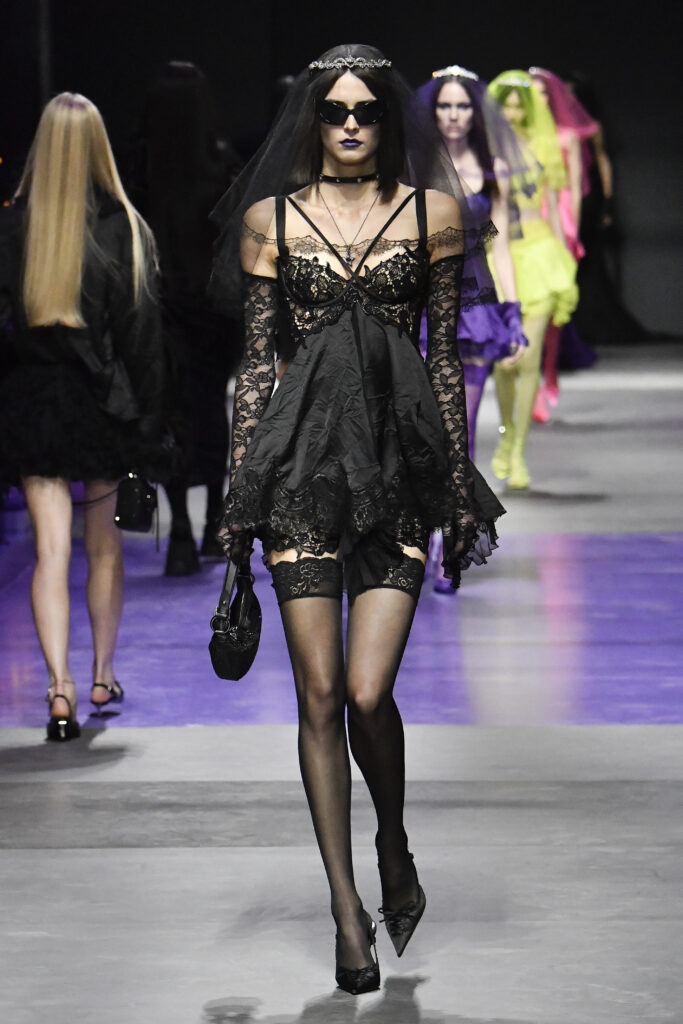 Podiumu žengiantis modelis, apsivilkęs juodą gotiško stiliaus suknelę