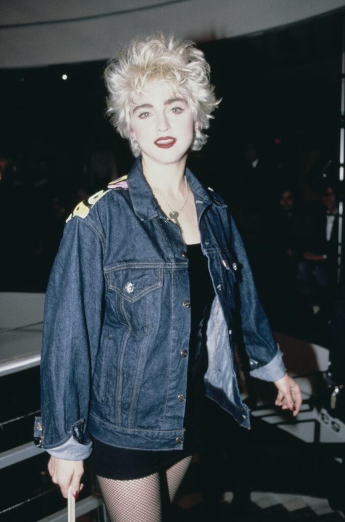 Madonna, dėvinti džinsinę striukę, mini sijoną ir tinklines pėdkelnes
