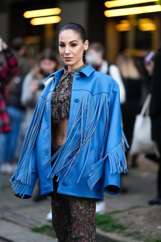Moteris, dėvinti mėlyną oversize odinę striukę su kutais ir trumpus gėlėtus marškinėlius
