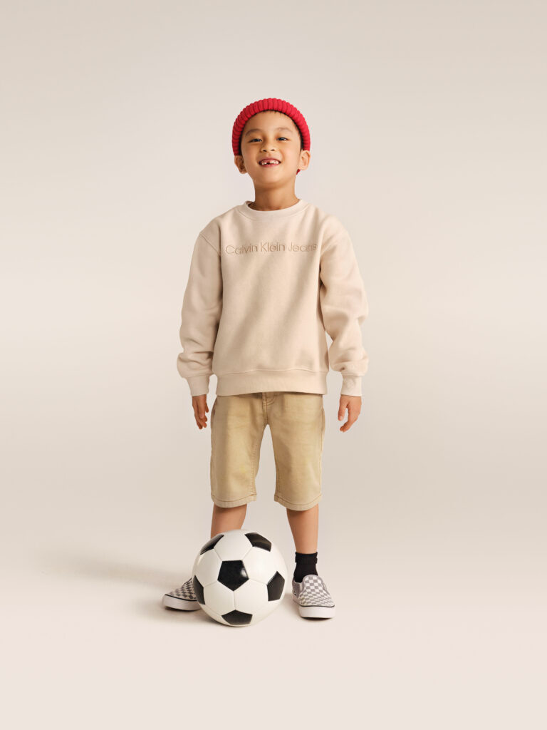 Berniukas, dėvintis smėlio spalvos Calvin Klein Jeans džemperį ir Vans sportbačius